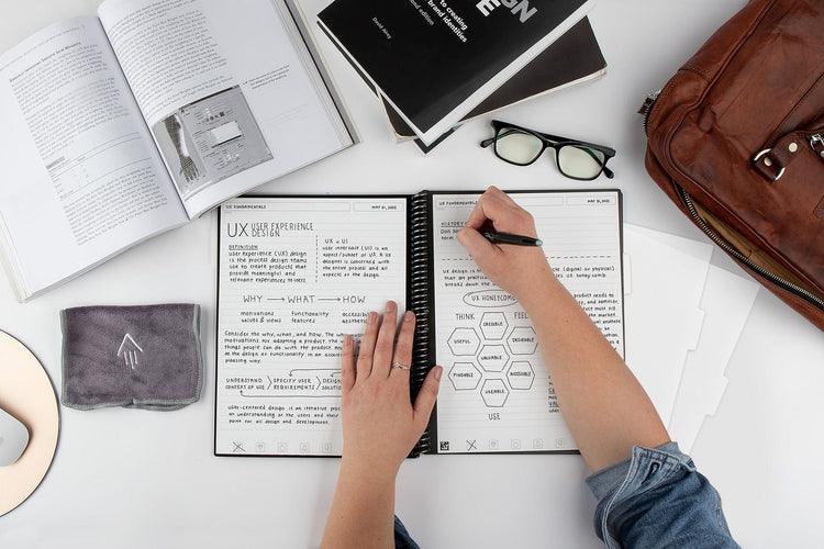 person writing in notebook on a desk